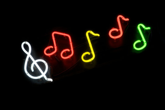 Musical notes with treble clef in colorful neon lights floating across dark background at night