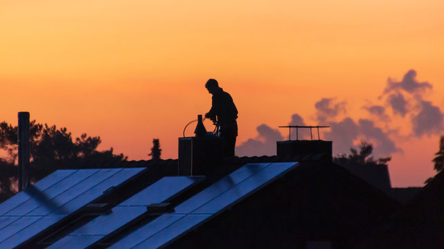 Männliche silhouette im Abentrort auf einem Dach bei reinigen des Schornstein