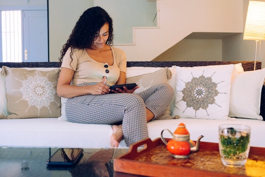 Ethnic woman isolated on the living room using technology at home. Communication and connecting people with electronic devices. Arab lifestyle. Muslim tea time. Internet and technologies concept.