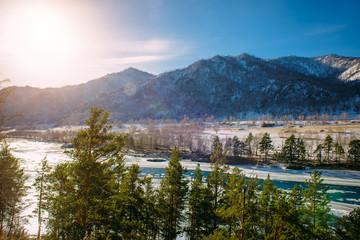 Beautiful winter landscape, mountain river valley in fantastic sunlight. Turquoise river runs among snow-covered banks with coniferous forest. Unfrozen area on the ice-bound mountain river.