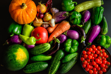 Harvest or Thanksgiving background with autumn vegetables on dark table. Seasonal ingredients for cooking: pumpkin, onions, carrots, eggplant, tomatoes, paprika, garlic, cucumbers. Top view, close-up.