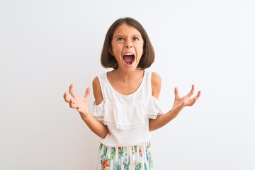 Young beautiful child girl wearing casual dress standing over isolated white background crazy and mad shouting and yelling with aggressive expression and arms raised. Frustration concept.