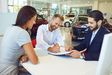 Smiling man and woman buys a car in a car showroom.