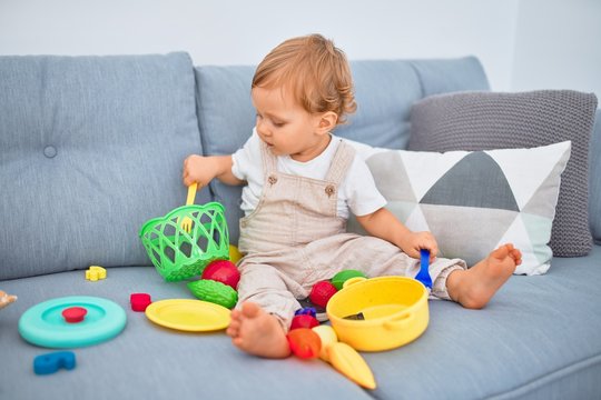 Adorable blonde toddler sitting on the sofa playing with plastic meals toys at home