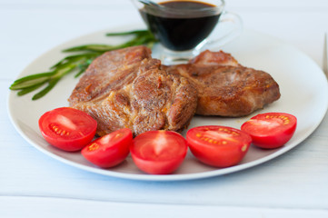 Tasty, juicy, fried meat steaks of pork or beef with sauce, spices and tomato on gray plate on a light background