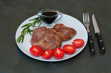 Juicy meat steaks with rosemary, sauce, tomatoes on a plate, on dark gray concrete background