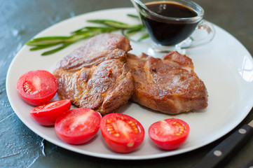 Fragrant pork meat steaks with spices, tomatoes and sauce, on a gray plate, on dark concrete background with place for text
