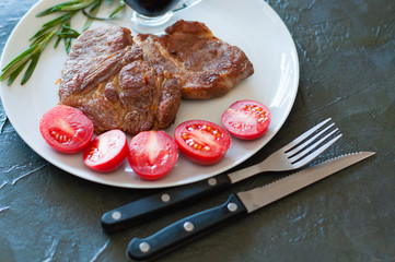 Juicy meat steaks of veal, beef or pork with rosemary, tomatoes and sauce, on gray plate, on a dark concrete background with copy space