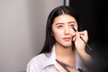 Beautiful young asian woman and professional makeup artists applies eye shadow. Beautiful woman face. Perfect makeup.