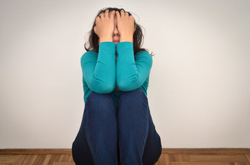 Depressed and sad woman covering her face with hands and sitting on the floor in the empty room
