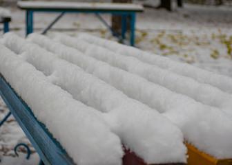 Park bench covered by snow. The first snow in the city. Cloudy snowy weather.