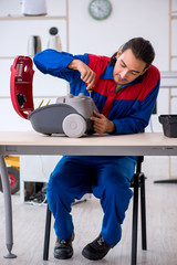 Young male contractor repairing vacuum cleaner at workshop