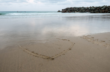 Heart drawn in the sand with people surfing in the background
