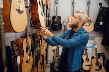 Bebaarde jonge man die een gitaar kiest in de muziekwinkel