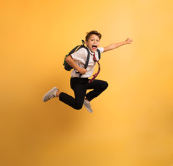 Fototapeta na wymiar Young boy student jumps high like a super hero. Yellow background
