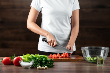 Woman cook cuts vegetables for salad preparation on a wooden background. Proper healthy eating.