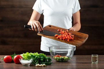 Woman cook cuts vegetables for salad preparation on a wooden background. Proper healthy eating.