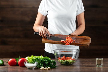 Woman cook cuts vegetables for salad preparation on a wooden background. Proper healthy eating.