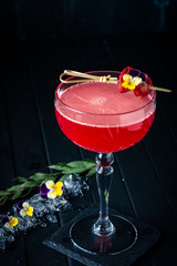 Strawberry red margarita alcoholic cocktail with tequila, liqueur and vermouth decorated with flowers on black wooden background
