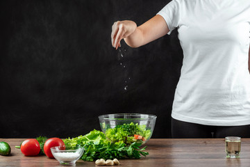 Woman cook salts vegetables, preparing salad on a wooden background. Proper healthy eating.