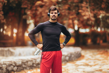 Portrait of  young man on a morning jogging in the autumn park, man listening to music with headphones