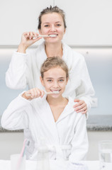 Fototapeta premium Happy mother and her daughter are brushing teeth with toothbrushes in the bathroom at home