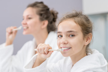 Mom and daughter brush their teeth in front of the bathroom mirror