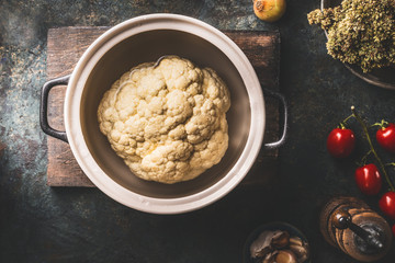 Whole cauliflower in cooking pot on dark rustic background with ingredients. Top view