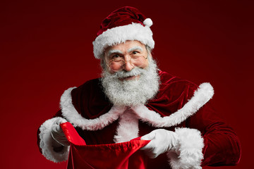 Waist up portrait of smiling Santa Claus holding sack with Christmas presents while standing over...