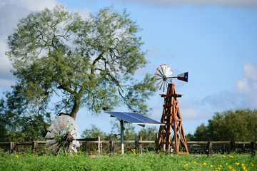 Solar Water well with Texas Windmill, in front of a green beautiful tree, with old vintage windmill on ground in front of fence.