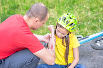Fototapeta na wymiar Sad girl shows her father wound on elbow after falling from a bicycle