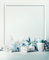 Frame of blue white beauty setting for spa, wellness or skin care concept. Burning candles with beautiful flowers, towels with cosmetic products for full feeling and relaxing standing on table