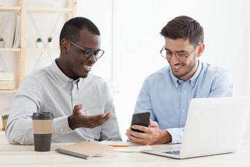 One colleague helping another with his task showing solution on smartphone at office desk