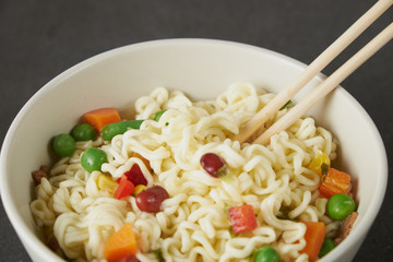 Hand uses chopsticks to pickup tasty noodles with steam and smoke in bowl on wooden background, selective focus. Asian meal on a table, junk food concept