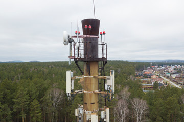 Mobile telephone network base station telecommunication tower with smart cellular antennas radiating and broadcasting a strong digital signal waves from the top. Against the forest