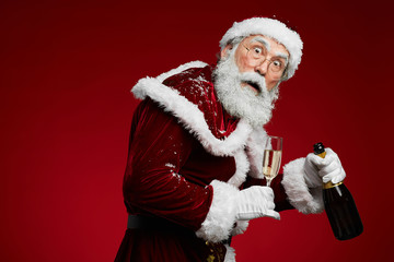 Waist up portrait of sneaky Santa Claus holding champagne standing against red background, copy space