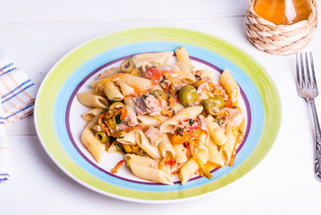 Italian cuisine - penne rigate pasta with tuna, olives and pepper sauce on a rustic plate on a light table with a fork and a bottle of olive oil