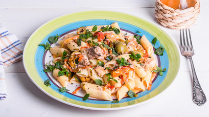 Italian cuisine - penne rigate pasta with sweet pepper sauce with tomatoes, tuna with olives closeup on a plate on a light wooden table