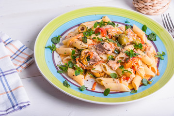 Italian cuisine - penne rigate pasta with sweet pepper sauce with tomatoes, tuna with olives on a plate on a light wooden table, top view