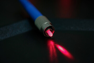 Closeup of connectors of optical fiber network cable. The laser shines from the optical cable.
