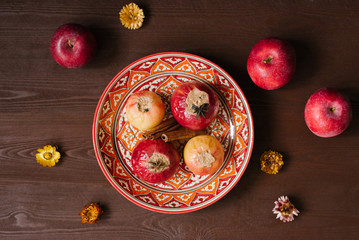 Baked apples with cottage cheese on a patterned red plate with an Uzbek pattern on a wooden brown background. Autumn menu