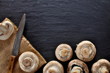 Edible half pieced mushrooms - champignons and rustic knife on vintage slate slab. Copyspace. Top view.