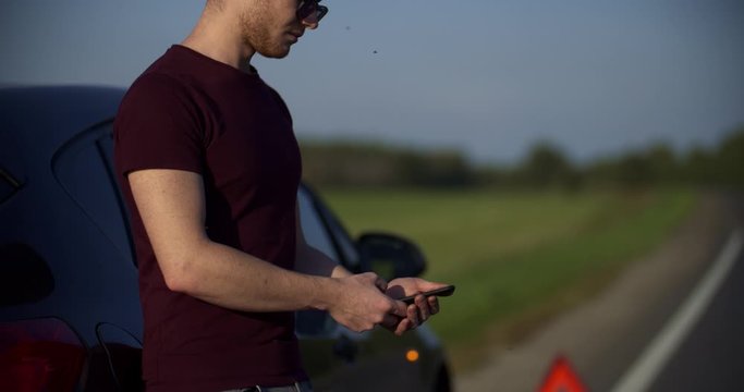crane shot of portrait of young man looks at something in the phone, a broken car on the road in the frame on the emergency