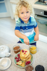 Little curly boy eating sweet pancakes