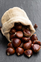 Fresh chestnut scattered of the burlap bag on black stone background