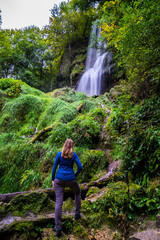 Germany, Young beautiful girl with long blond hair amazed by the beauty of nature at waterfall in green forest of bad urach