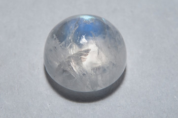 Cabochon cut adular moonstone displaying a prominent blue schiller effect, a play of light within its translucent body, showing internal inclusions and a smooth, polished surface on neutral background