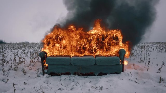 A sofa burns in the winter field. The furniture is on fire. Concept video