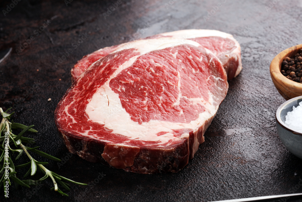 Wall mural Raw fresh meat Ribeye Steak, seasoning and meat fork on rustic background