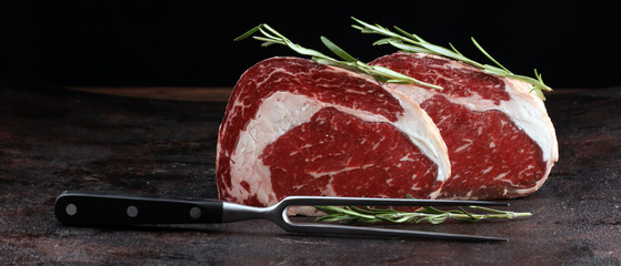 Raw fresh meat Ribeye Steak, seasoning and meat fork on rustic background